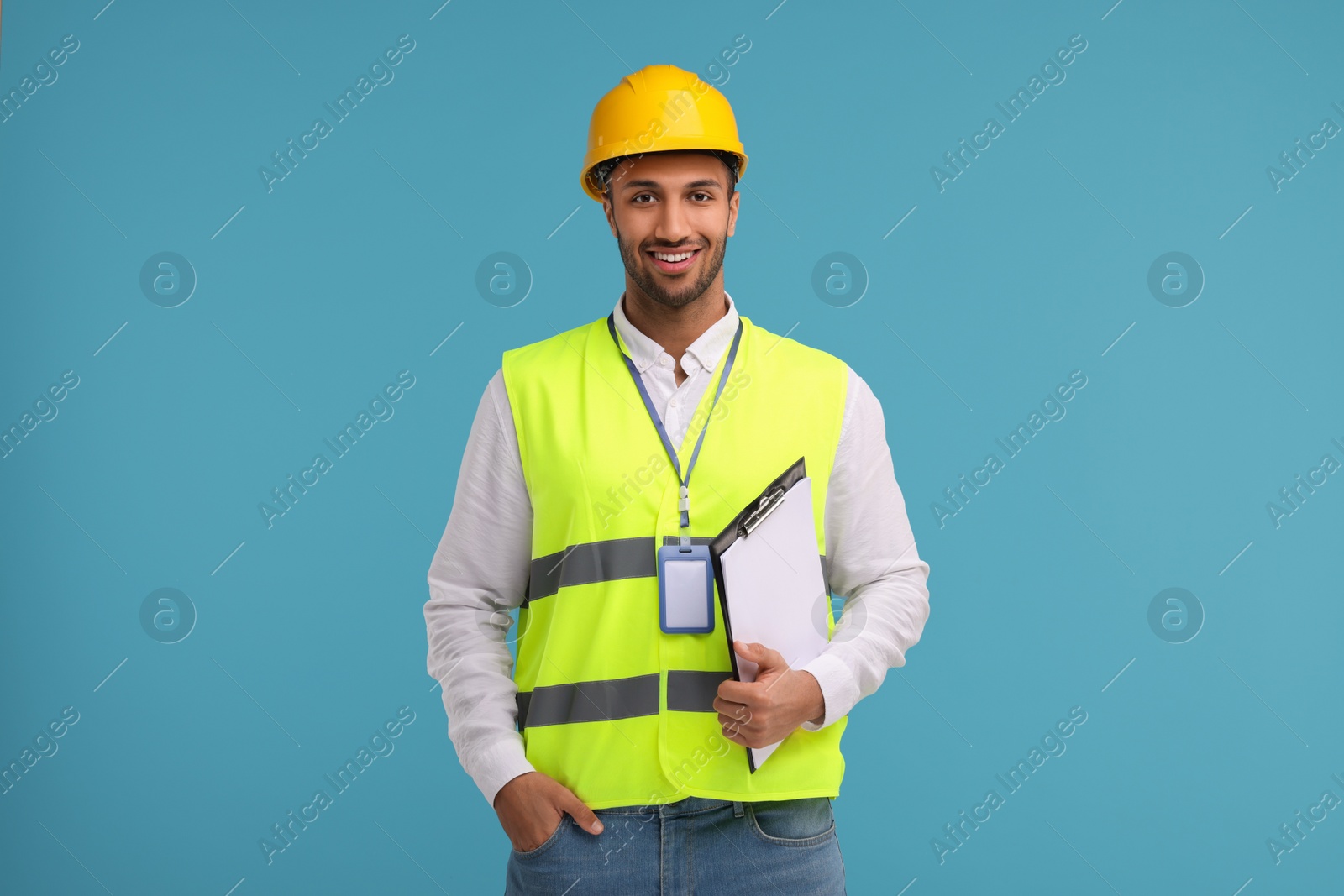 Photo of Engineer in hard hat holding clipboard on light blue background