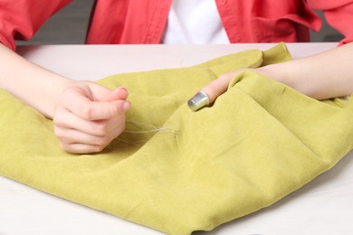 Photo of Woman with sewing thread embroidering on cloth at white table, closeup