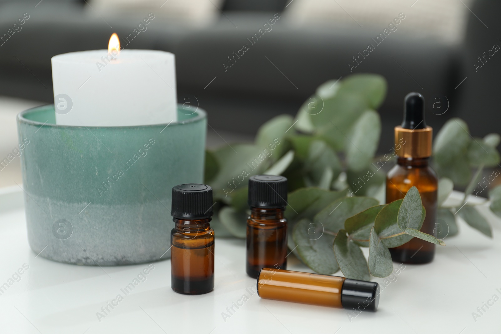 Photo of Aromatherapy. Bottles of essential oil, burning candle and eucalyptus leaves on white table