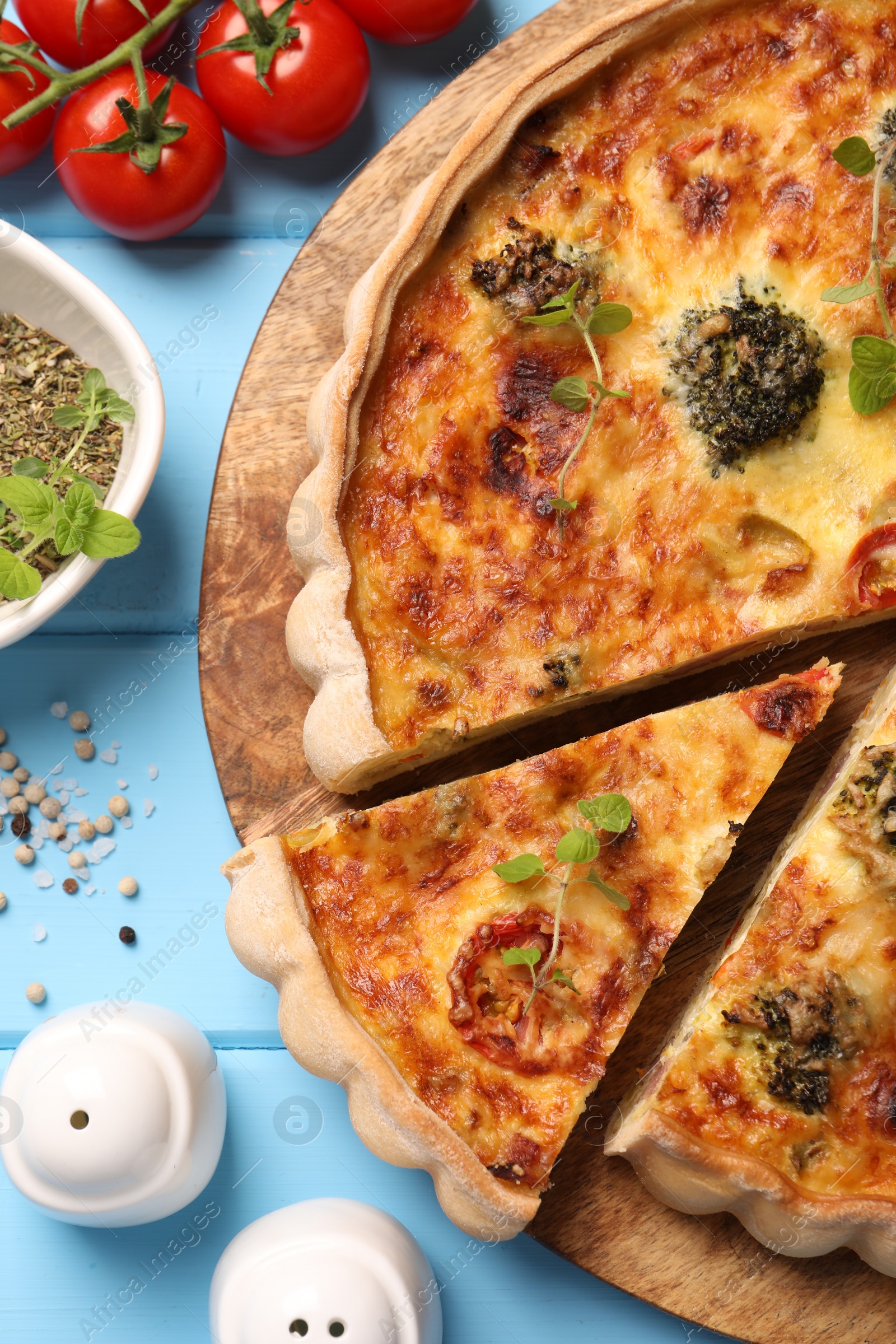 Photo of Delicious homemade vegetable quiche and ingredients on light blue wooden table, flat lay