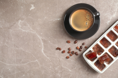 Photo of Ice cubes, cup of coffee and beans on grey table, flat lay. Space for text