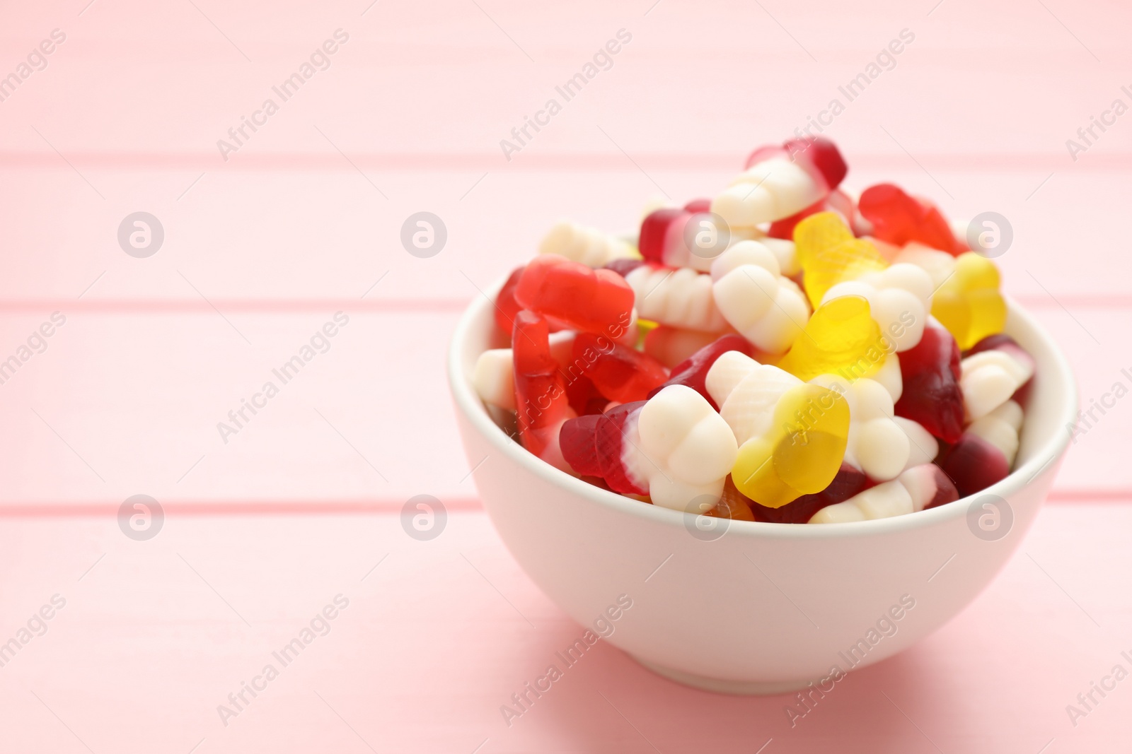 Photo of Delicious gummy ice cream cones shaped candies on pink wooden table. Space for text