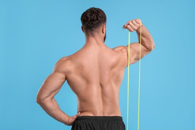 Young man exercising with elastic resistance band on light blue background, back view