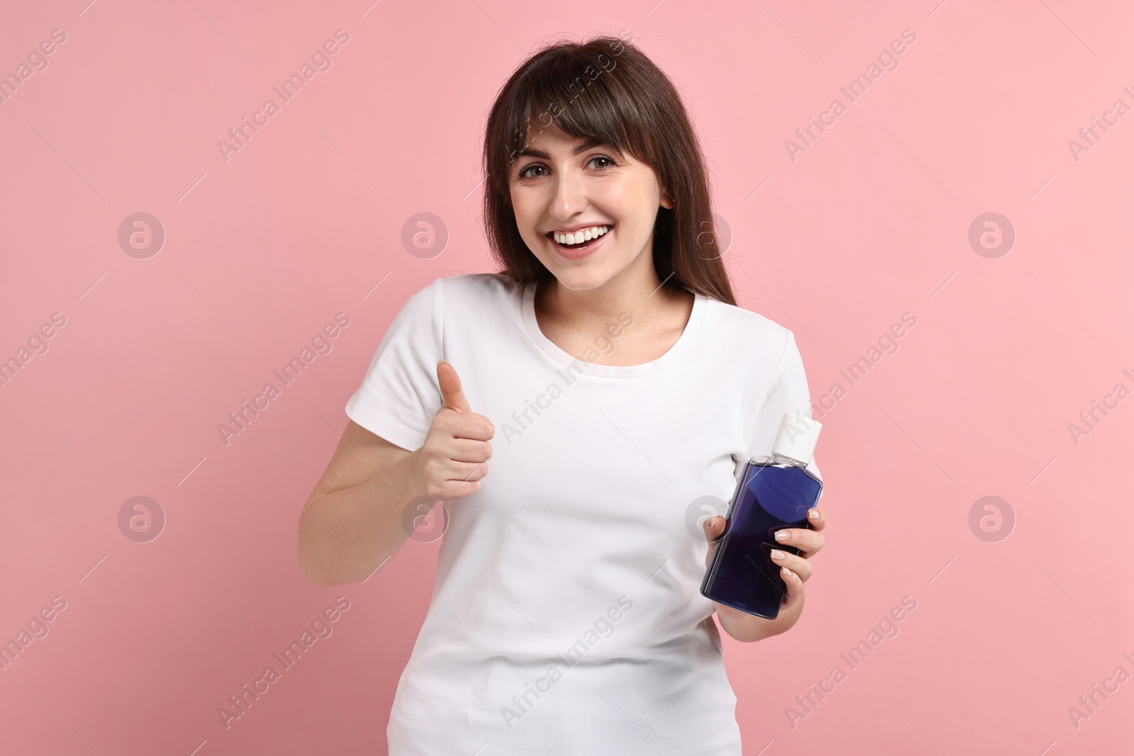 Photo of Young woman with mouthwash showing thumbs up on pink background