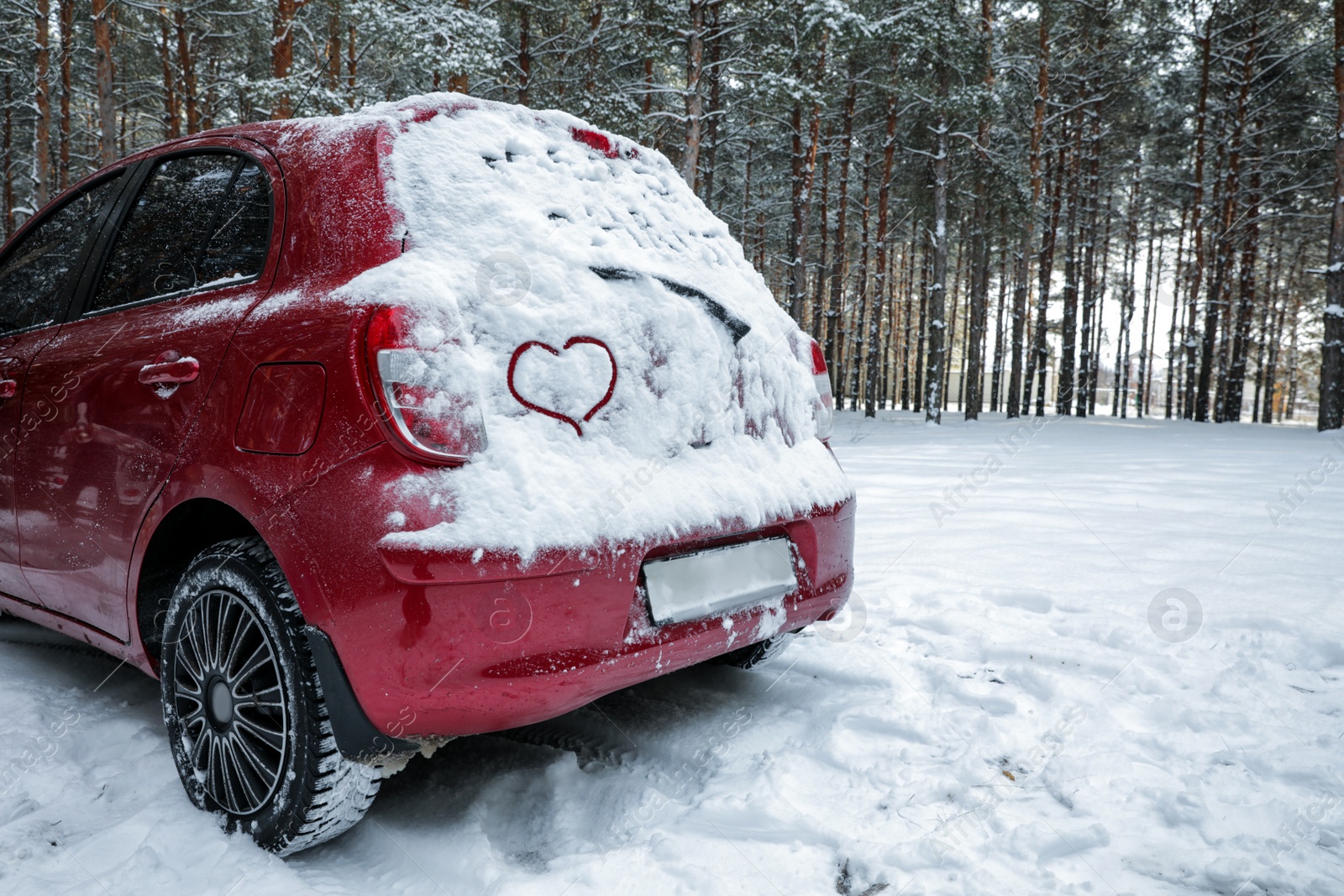 Photo of Heart drawing on snow covered car in winter forest. Space for text