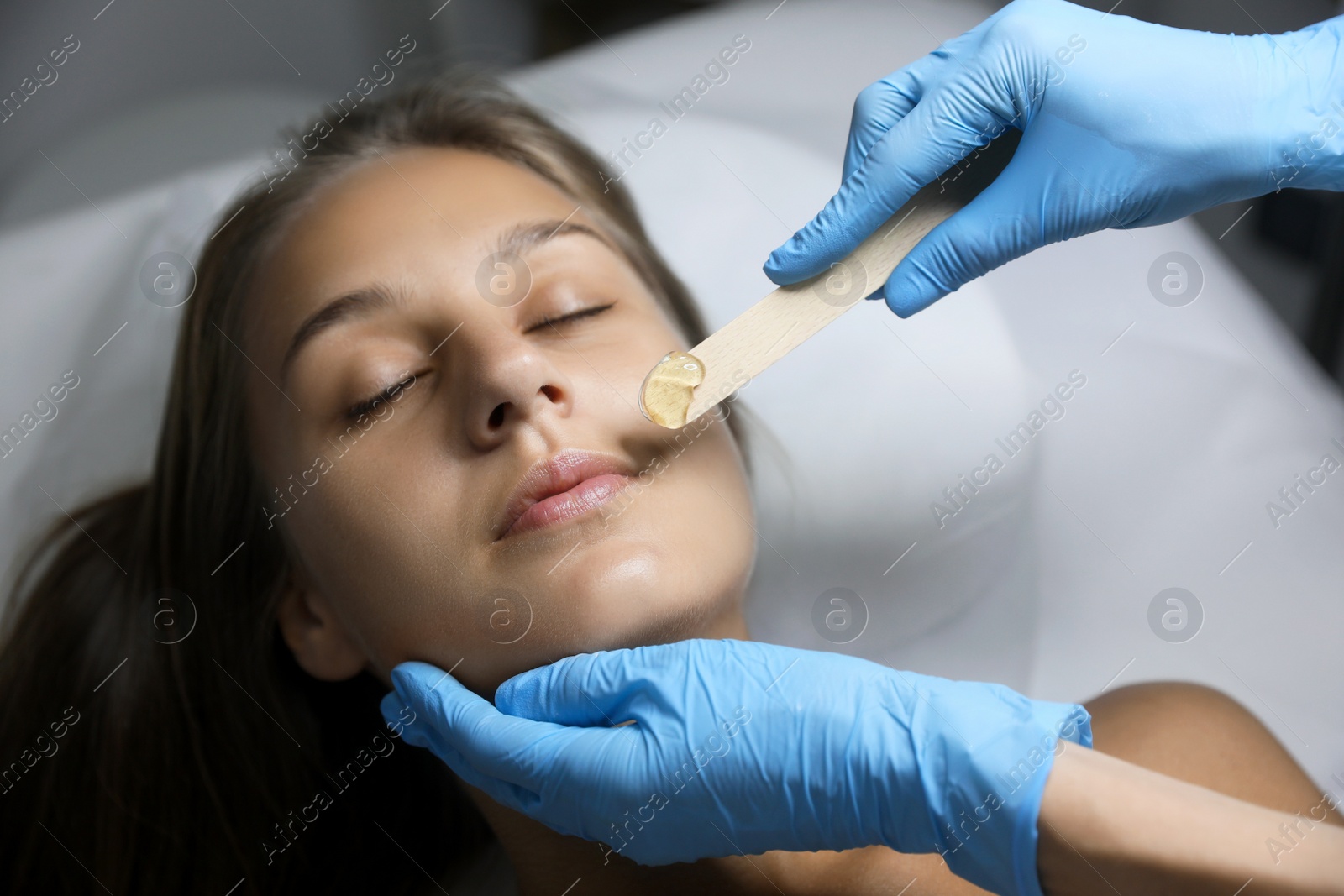 Photo of Young woman undergoing hair removal procedure on face with sugaring paste in salon
