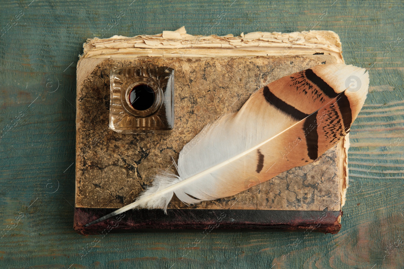 Photo of Feather pen, inkwell and book on blue wooden table, top view