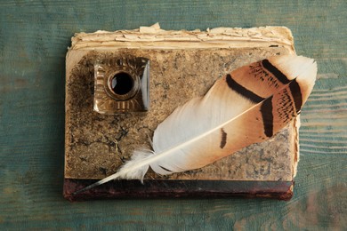 Feather pen, inkwell and book on blue wooden table, top view