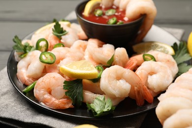 Photo of Tasty boiled shrimps with cocktail sauce, chili, parsley and lemon on table, closeup