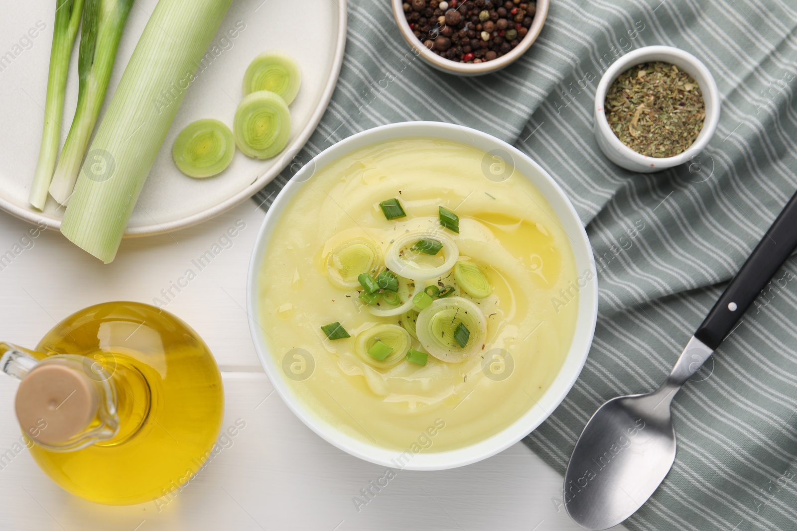 Photo of Bowl of tasty cream soup with leek and spoon on white wooden table, flat lay