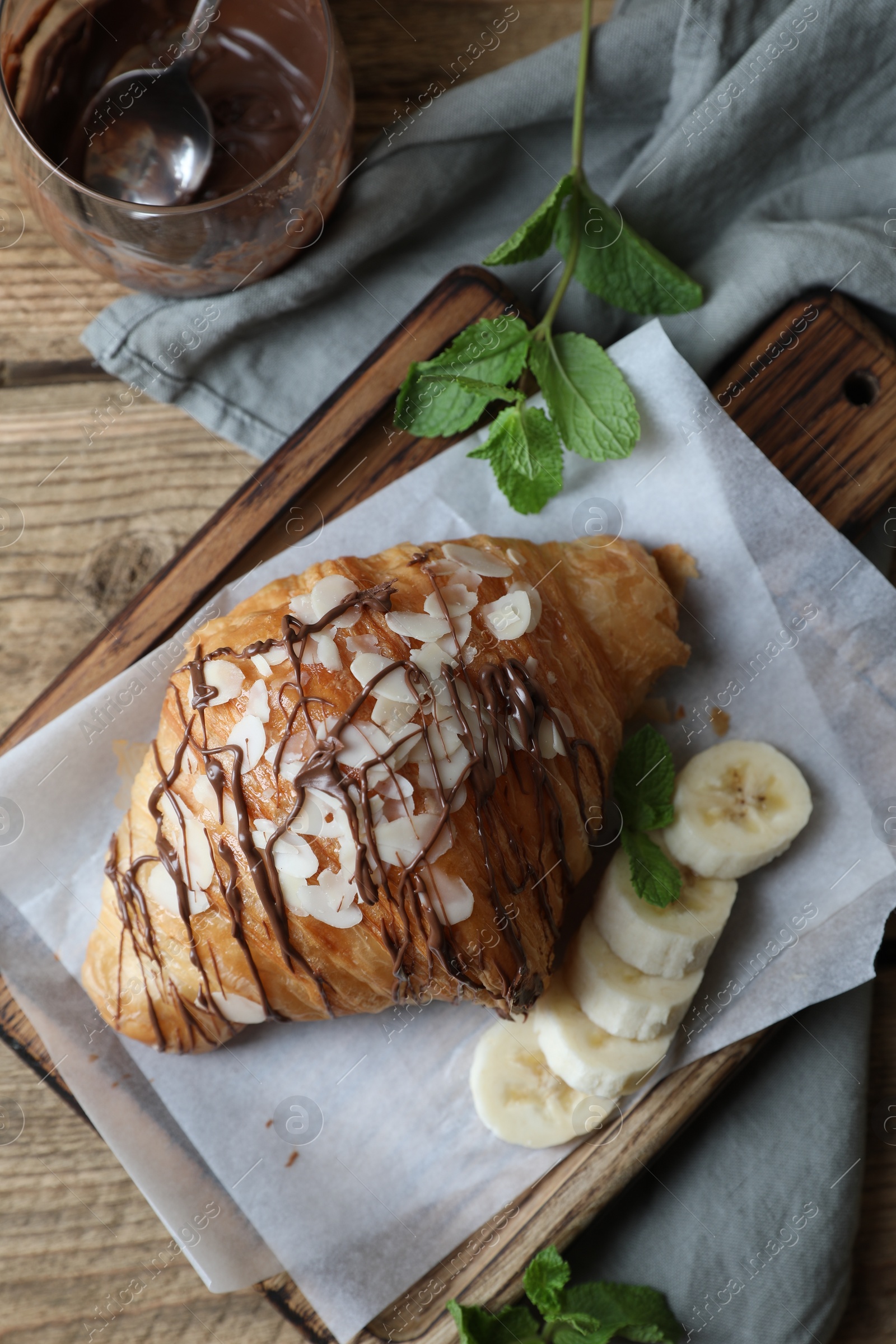 Photo of Delicious croissant with chocolate and banana on wooden table, flat lay