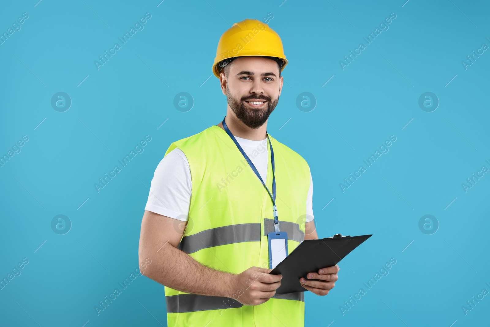 Photo of Engineer in hard hat holding clipboard on light blue background