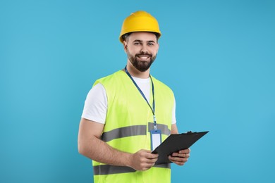 Photo of Engineer in hard hat holding clipboard on light blue background