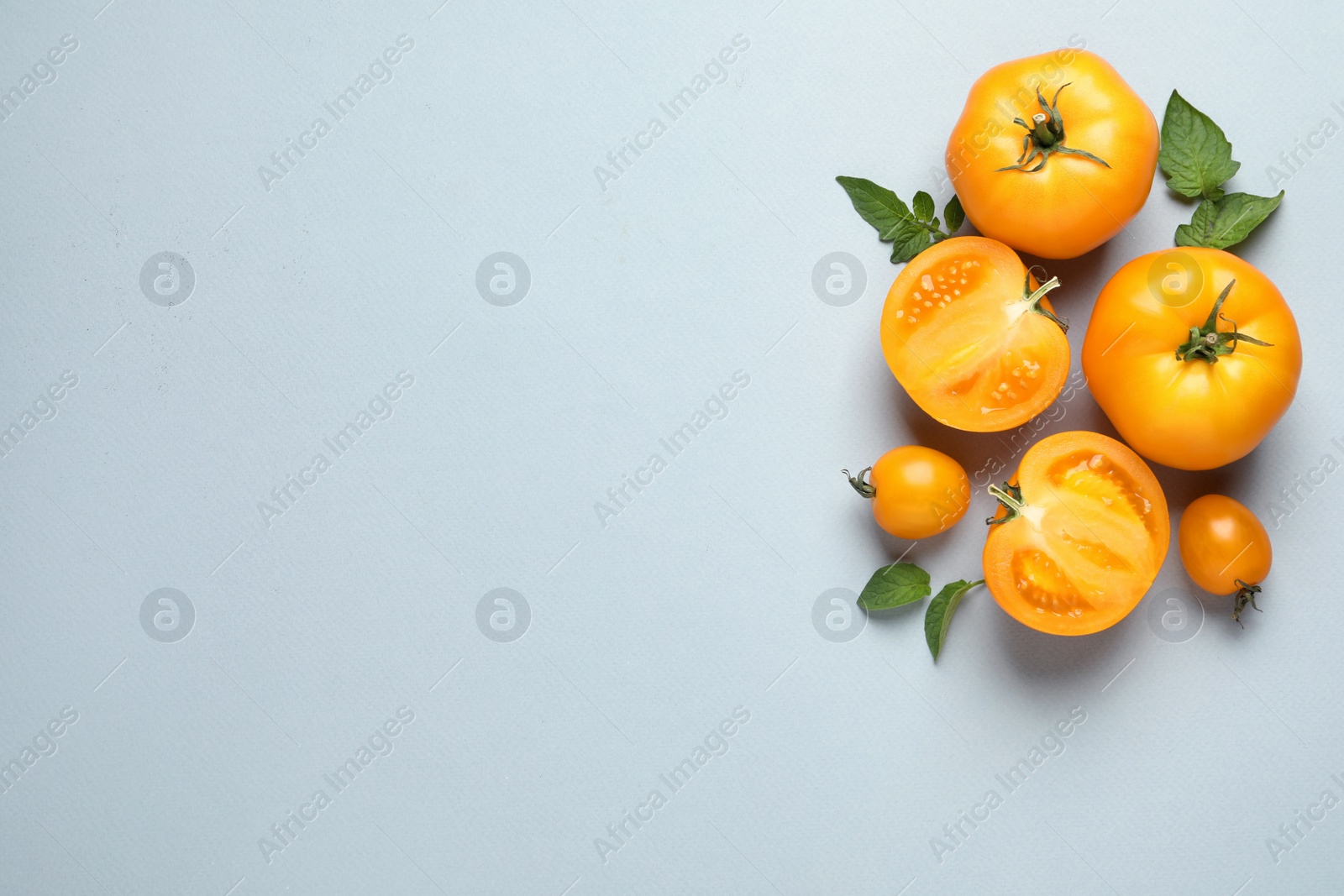 Photo of Cut and whole ripe yellow tomatoes with leaves on light background, flat lay. Space for text