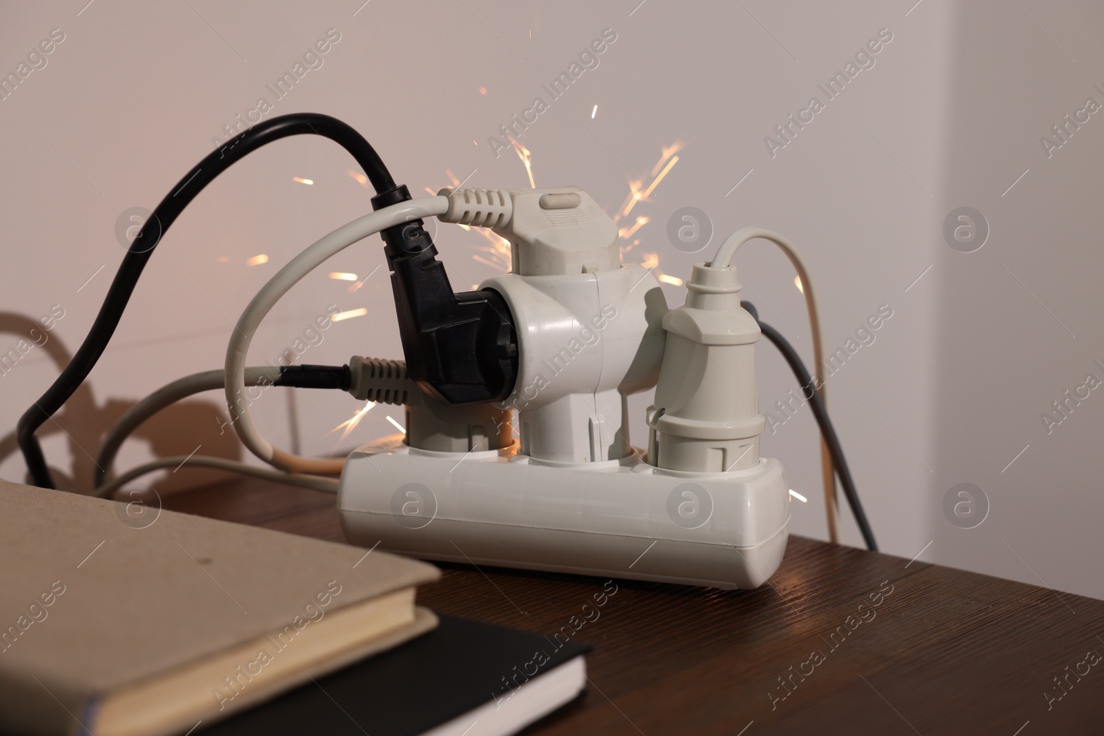 Photo of Inflamed plug in power strip indoors on wooden table. Electrical short circuit