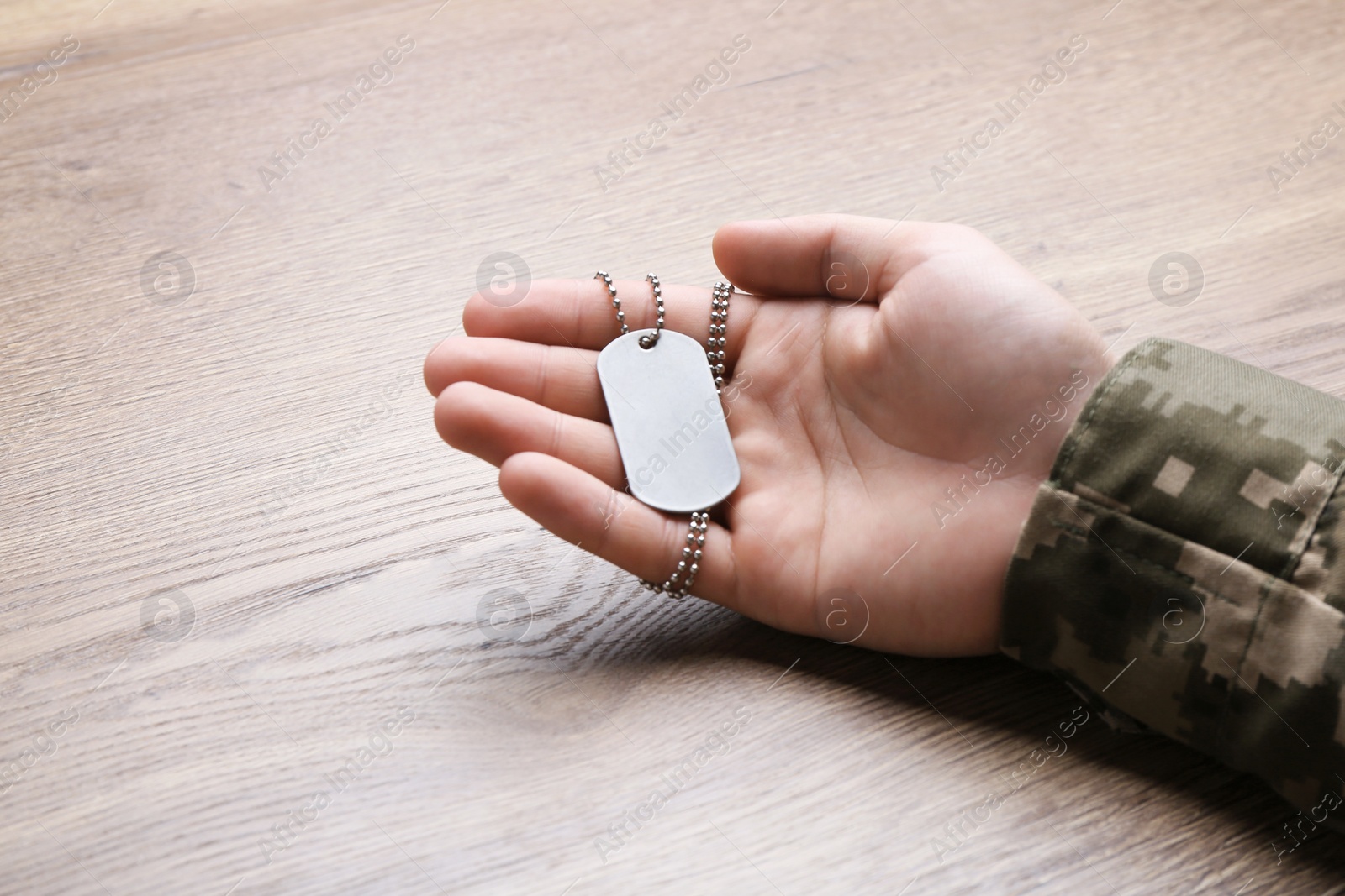 Photo of Man in camouflage uniform holding military ID tag over wooden background, closeup