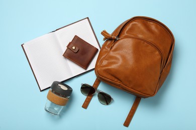 Photo of Stylish urban backpack with different items on light blue background, flat lay