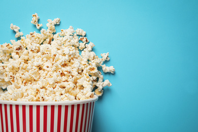 Photo of Overturned paper bucket with delicious popcorn on light blue background, top view. Space for text