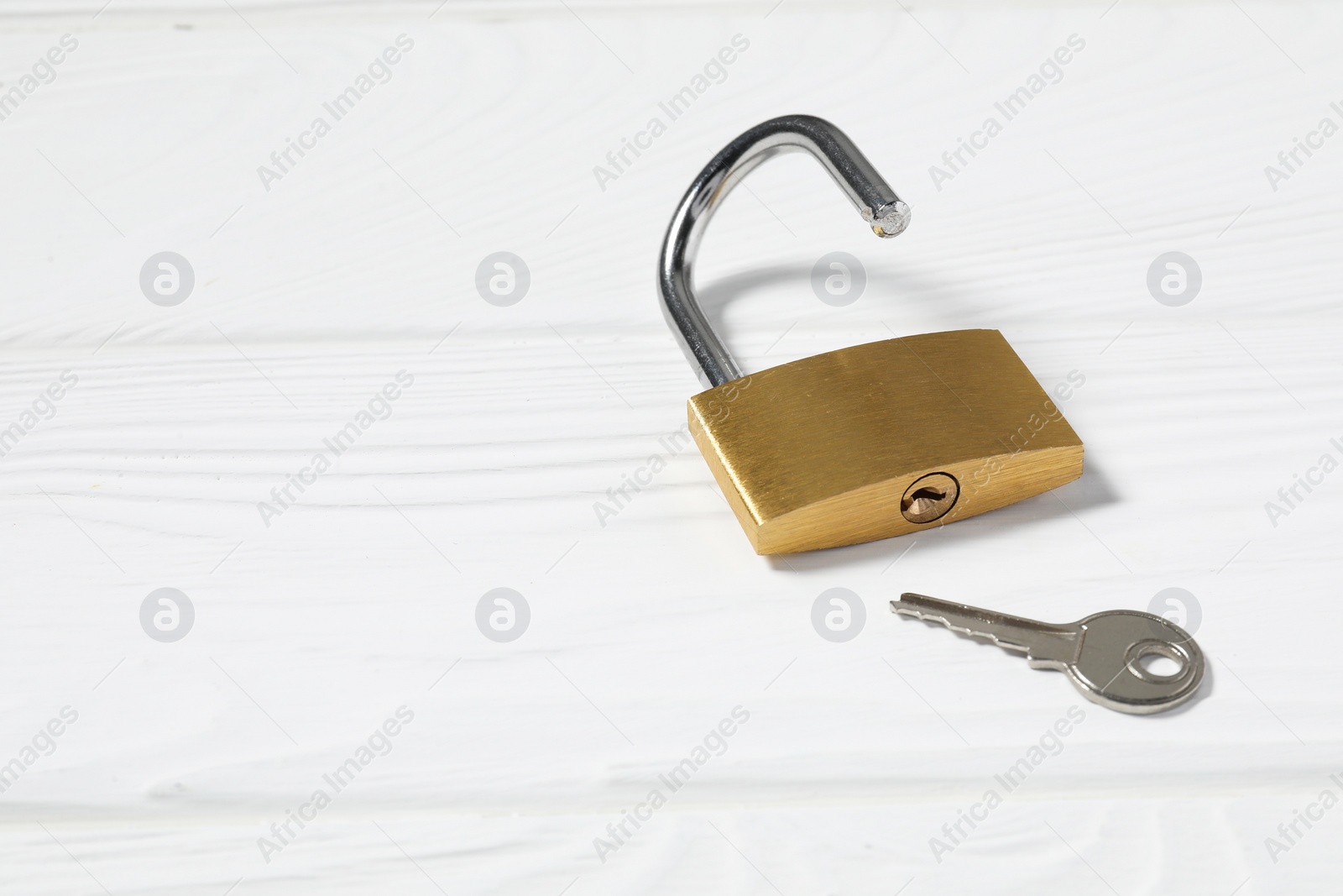 Photo of Steel padlock with key on white wooden table. Space for text