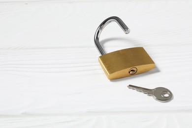 Photo of Steel padlock with key on white wooden table. Space for text