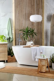 Modern white tub and beautiful green houseplants in bathroom. Interior design