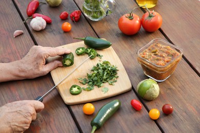 Photo of Woman cutting pepper for tasty salsa sauce at wooden table