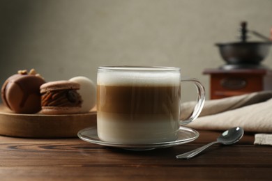 Photo of Aromatic coffee in cup, macarons and spoon on wooden table