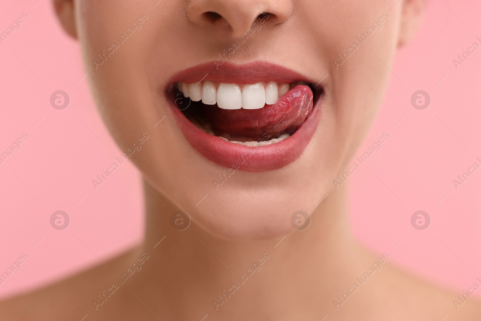 Photo of Woman with beautiful lips licking her teeth on pink background, closeup