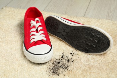 Photo of Red sneakers and mud on beige carpet, closeup