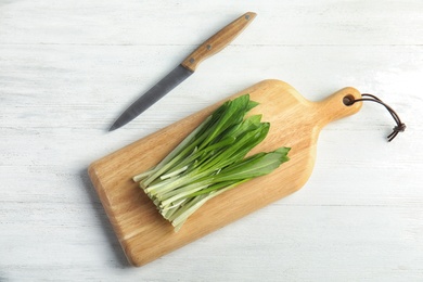 Photo of Board with wild garlic or ramson and knife on white wooden table, flat lay