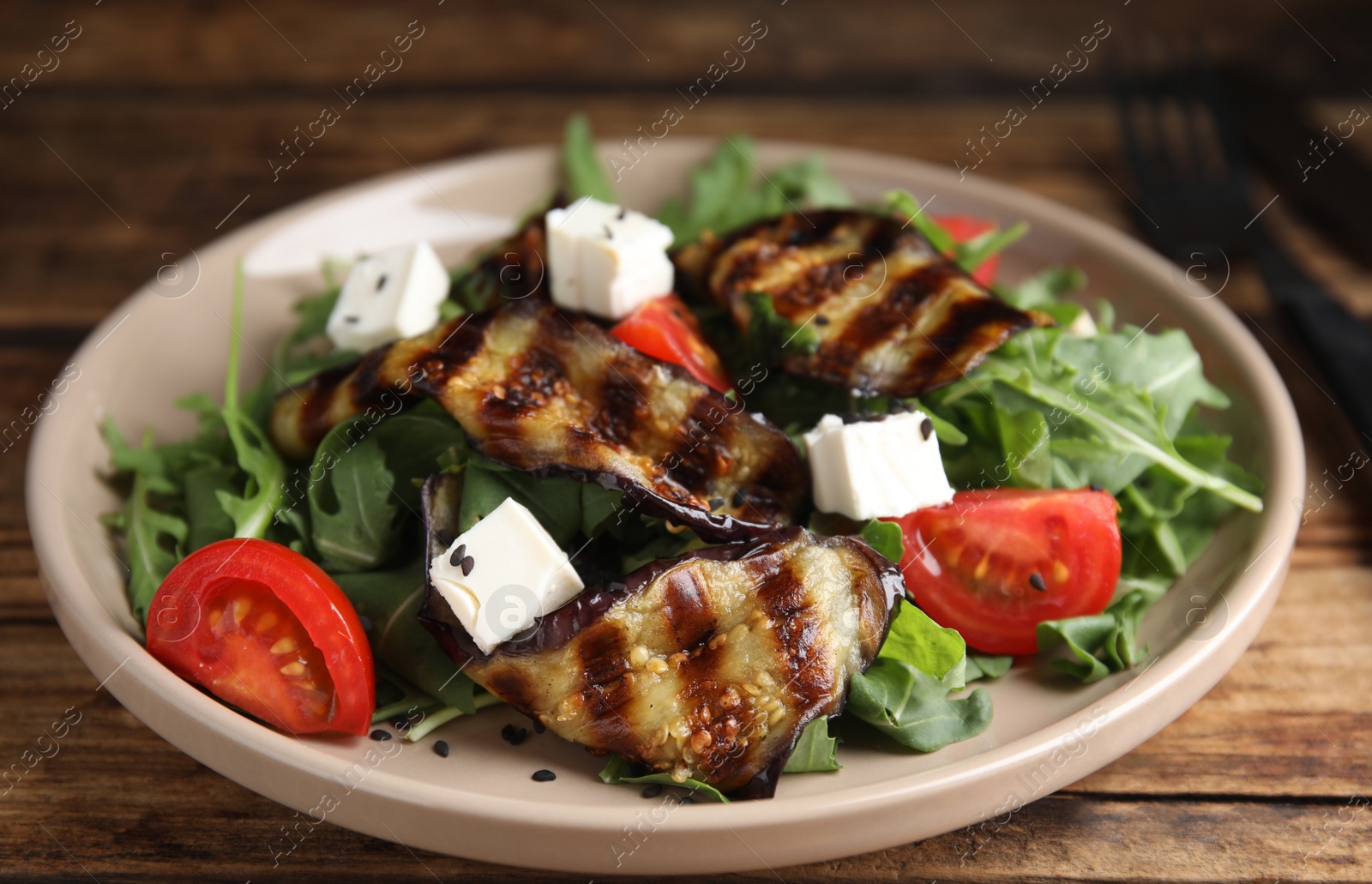 Photo of Delicious salad with roasted eggplant, feta cheese and arugula served on wooden table, closeup