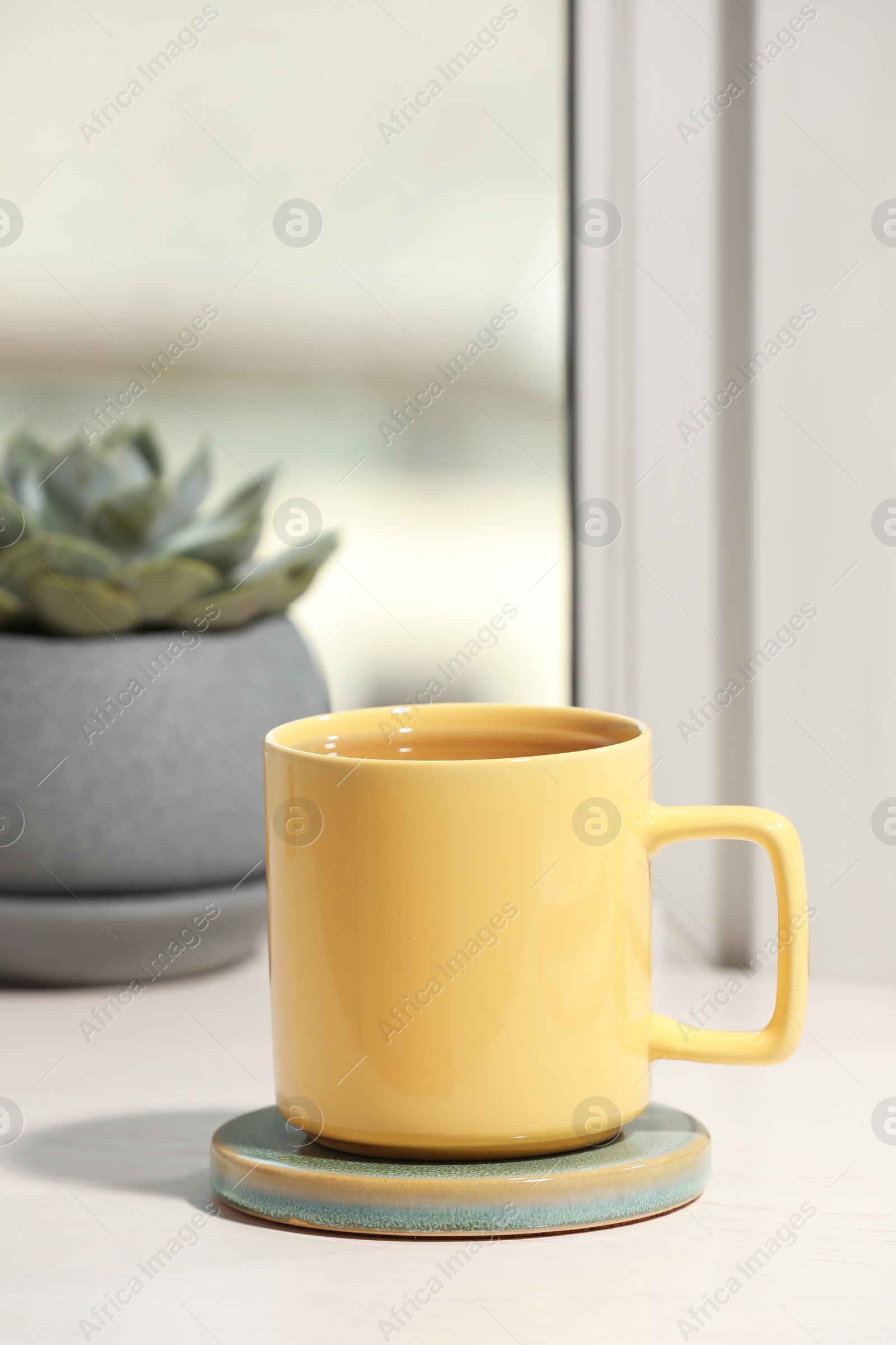 Photo of Yellow cup of tea and succulent on wooden window sill