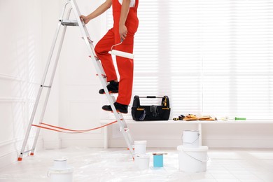 Worker with roller climbing up ladder indoors, closeup. Space for text