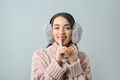 Beautiful young woman wearing earmuffs on light grey background