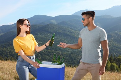 Couple and cool box with bottles of beer in mountains