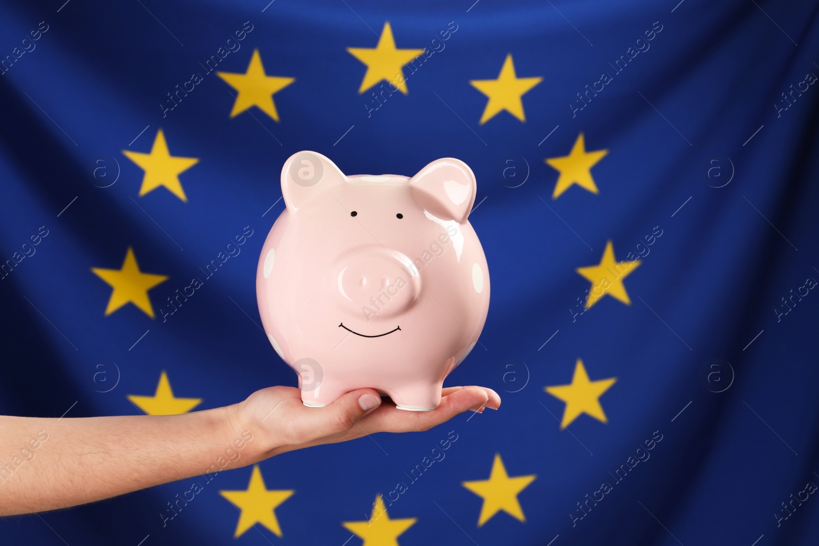 Photo of Woman holding pink piggy bank against flag of European Union, closeup