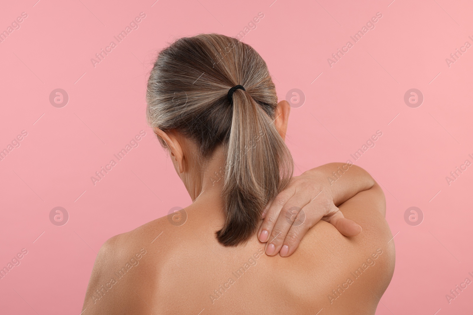 Photo of Woman suffering from pain in her neck on pink background, back view