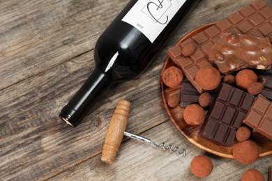 Bottle of red wine, chocolate sweets and corkscrew on wooden table, above view. Space for text