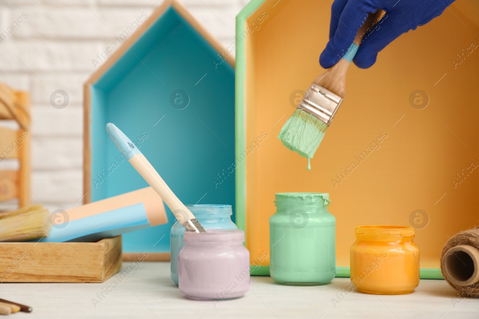 Photo of Decorator dipping brush into jar of green paint at white table, closeup