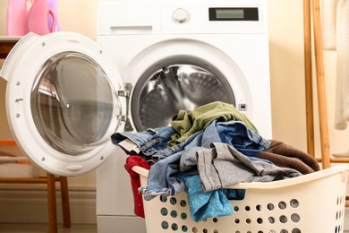 Photo of Basket with dirty laundry near washing machine indoors