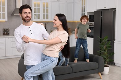 Happy family having fun at home. Couple dancing while children jumping on sofa