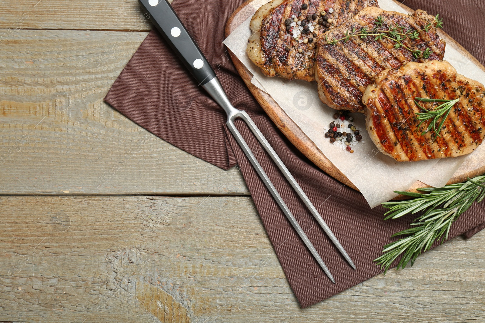 Photo of Delicious grilled pork steaks with herbs, spices and carving fork on wooden table, top view. Space for text