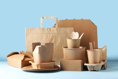 Photo of Eco friendly food packaging. Paper containers, tableware and bag on white table against light blue background