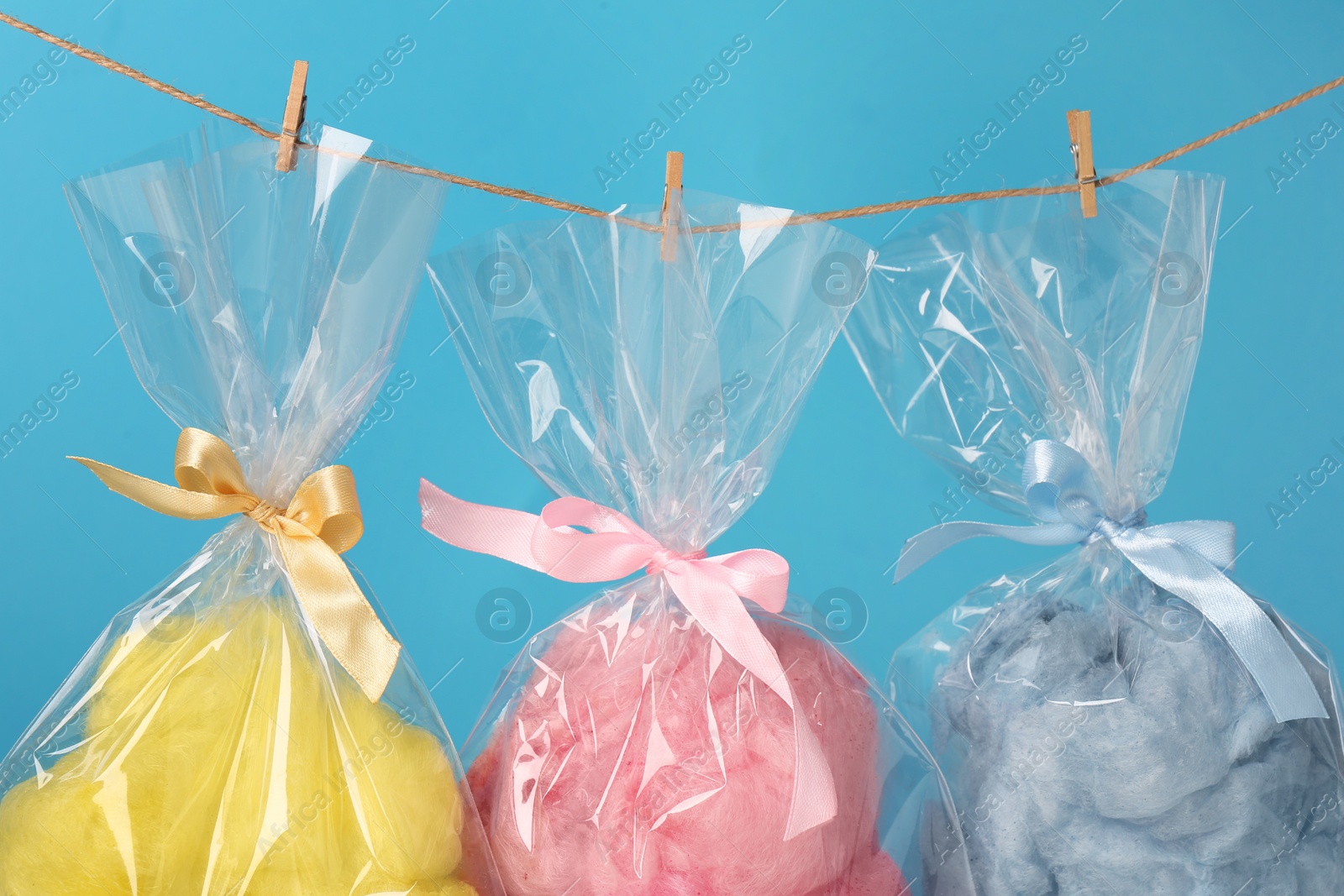 Photo of Packaged sweet cotton candies hanging on clothesline against light blue background, closeup