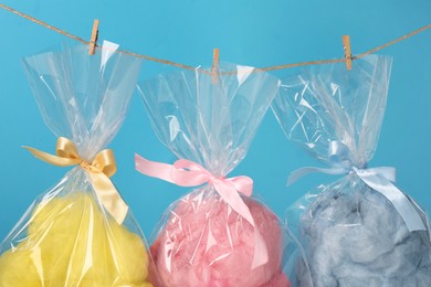 Photo of Packaged sweet cotton candies hanging on clothesline against light blue background, closeup