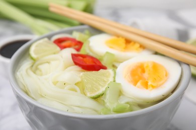 Bowl of delicious rice noodle soup with celery and egg on white table, closeup