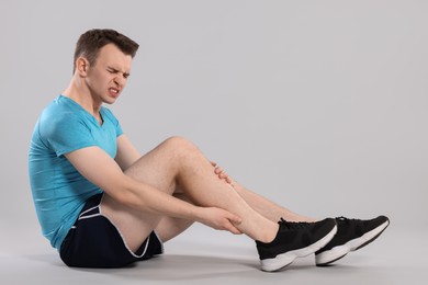 Man suffering from leg pain on grey background