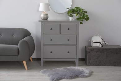 Stylish room interior with round mirror on wall over chest of drawers