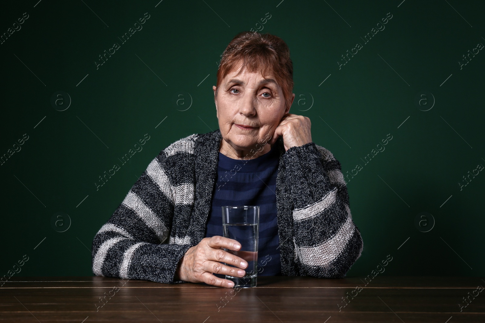Photo of Poor senior woman with glass of water sitting at table against color background