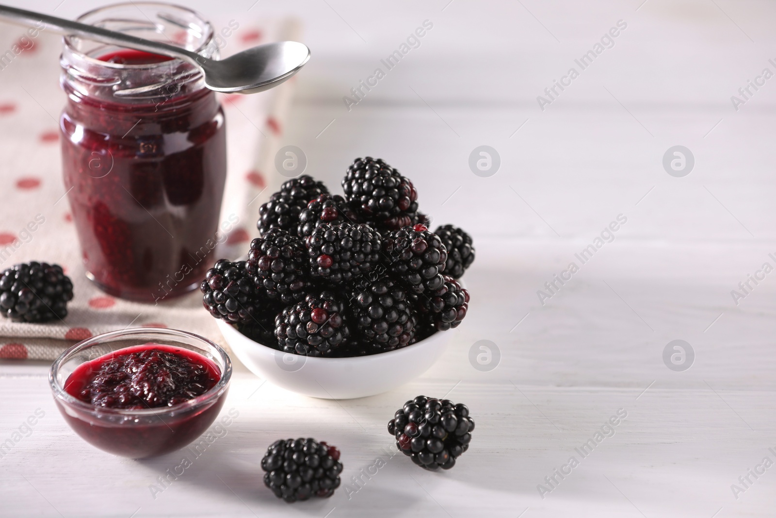 Photo of Fresh ripe blackberries and tasty jam on white wooden table. Space for text